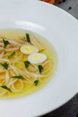 Az yağlı tavuk çorbası, yarı pişmiş yumurta ve maydanozla birlikte beyaz arka planda izole edilmiş cam bir kasede. Yüksek kalite fotoğraf