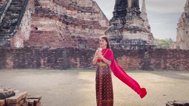 身着传统的红色泰式服装和金色饰物的年轻女子站在古老的华特朝瓦那罗寺前 被视为一种欢迎和问候 泰国民族服装 — 图库视频影像