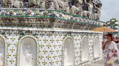 Aksesuarlı Tayland elbisesi giyen genç bir kadın Wat Arun Ratchawararam 'da elinde antika şemsiye ve çanta ile ayakta duruyor. Bangkok, Tayland