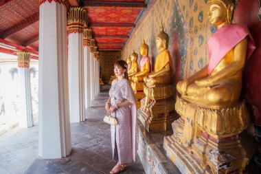 Birçok Buda heykelinin sıralandığı Wat Arun Ratchawararam 'da aksesuarlı Tayland elbisesi giyen genç bir kadın dünya turistleri için popüler bir yerdir. Bangkok, Tayland