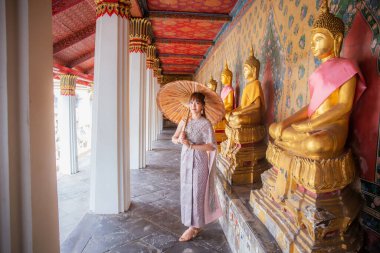 Geleneksel Tayland elbisesi ve aksesuarları içindeki genç kadın Wat Arun 'da birçok Buda heykelinin dizildiği bir şemsiye tutuyor. Burası dünya çapında turistler için popüler bir yerdir. Bangkok, Tayland