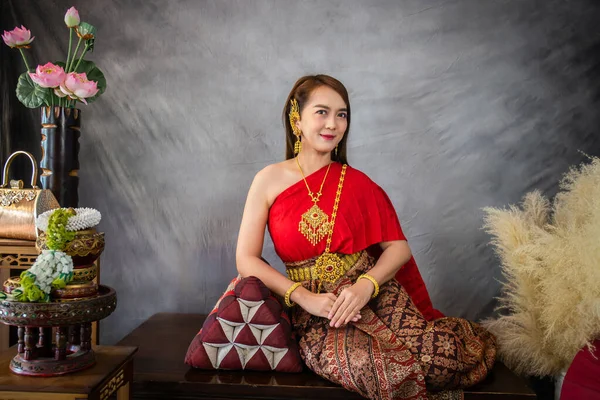 身穿传统红色泰国服装和金色装饰品的年轻女子坐在木制椅子上的枕头上 泰国民族服装 — 图库照片