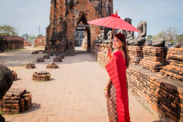 Geleneksel kırmızı Tayland elbisesi ve altın aksesuarları giyen genç kadın, tarihi Wat Chaiwatthanaram Ayutthaya sitesinde geleneksel bir şemsiye tutuyor. Tayland ulusal kostümü