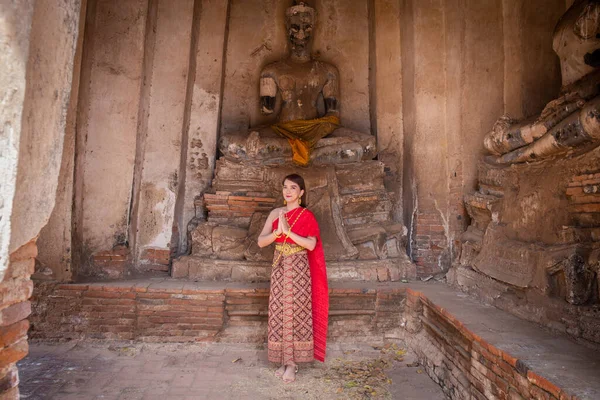 身着传统的红色泰式服装和金色饰物的年轻女子站在古埃及的一个巨大的佛塔前 作为欢迎和问候 Wat Chaiwatthanaram Ayutthaya — 图库照片