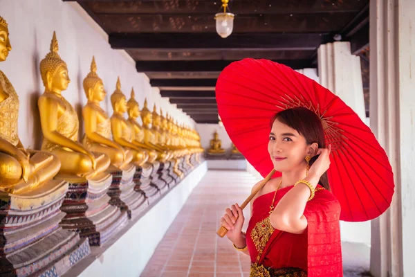 在历史名胜古迹Wat Phutthaisawan Ayutthaya 身穿传统红色泰式服装 头戴金色饰物的年轻女子手持传统雨伞站在那里 泰国民族服装 — 图库照片