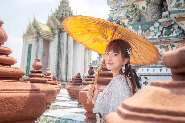 身穿传统泰国服装的年轻女子手持一把古老的雨伞站在世界各国游客最喜爱的目的地 瓦特阿伦 Wat Arun 泰国曼谷 — 图库照片