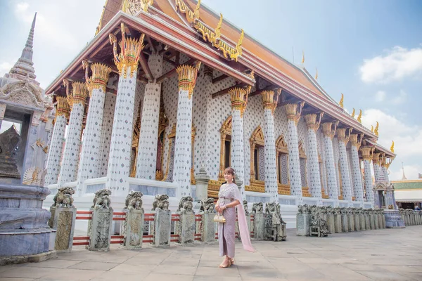 在Wat Arun Ratchawararam 身穿泰式连衣裙 头戴配饰 提着一个包的年轻女子这是个深受世界各地游客欢迎的目的地 泰国曼谷 — 图库照片