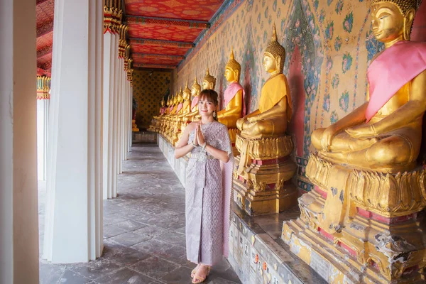 Tayland elbiseli ve aksesuarlı genç bayan, birçok Buda heykelinin sıralandığı Wat Arun 'da bir karşılama töreni düzenliyor. Burası dünya çapında turistler için popüler bir yerdir. Bangkok, Tayland