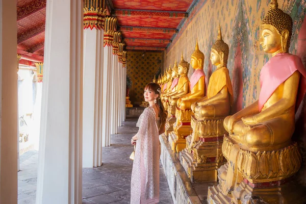 在许多佛像横行的地方 身穿泰式连衣裙 头戴配饰 提着一个包的年轻女子在Wat Arun Ratchawararam 泰国曼谷 — 图库照片