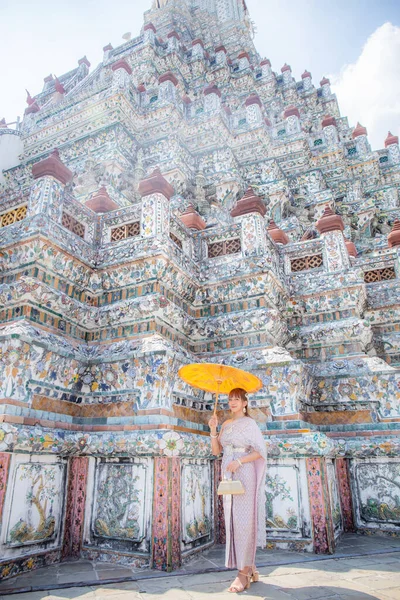 在Wat Arun Ratchawararam酒店 身穿泰式服装 头戴配饰的年轻女子手持古式雨伞和手提包 泰国曼谷 — 图库照片