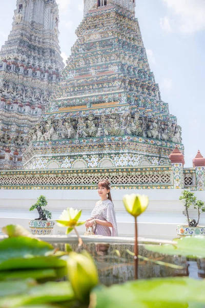 在Wat Arun Ratchawararam 一位身穿泰式连衣裙 头戴配饰 提着一个包的年轻女子面前有一朵莲花 它是世界各国游客的热门旅游胜地 泰国曼谷 — 图库照片