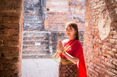 Geleneksel kırmızı Tayland elbisesi ve altın süslemeleri giymiş genç bir kadın Wat Chaiwatthanaram, Ayutthaya, Tayland 'daki antik sitede karşılama ve karşılama için bekliyor.
