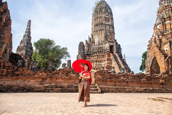 Geleneksel kırmızı Tayland elbisesi ve altın aksesuarları giyen genç kadın Wat Chaiwatthanaram, Ayutthaya, Tayland 'daki tarihi mekanda geleneksel bir şemsiye tutuyor.