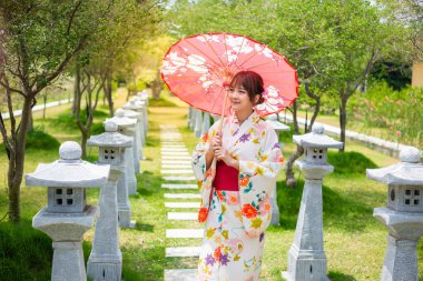 Geleneksel Japon kimonosu giyen genç bir kadın ya da torii sırıkları olan bir bahçede şemsiye tutan yukata..