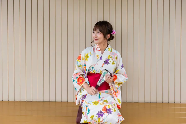 Молодая Женщина Традиционном Японском Кимоно Держит Бумажный Вентилятор Сидя Деревянном — стоковое фото
