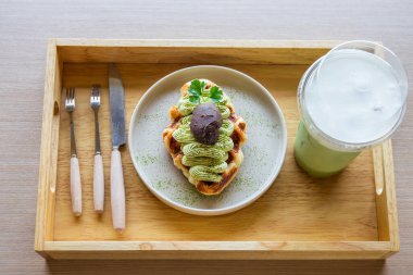 Japon geleneksel ahşap tepsisinde, çatal bıçak takımı ve buzlu yeşil çay eşliğinde, beyaz bir tabakta yeşil waffle 'lar..