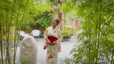 Japon kimonosu giyen bir kadın yeşil bambu orman parkında yürüyor.