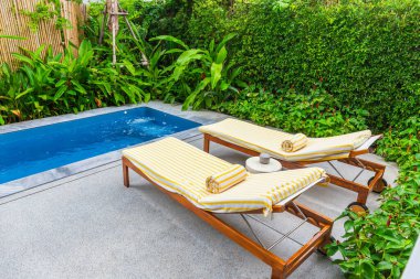 Havuz sandalyeleri ve arkasında yeşil ağaç olan güzel mavi su..