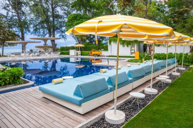 Şemsiyeli havuz sandalyeleri ve arka planda ağaç mavisi gökyüzü olan deniz kenarındaki güzel su yansımaları..