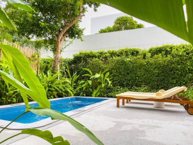 Havuz sandalyeleri ve arkasında yeşil ağaç olan güzel mavi su..