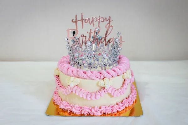 Pink and white cake with a birthday sign and a beautiful silver crown. Select focus