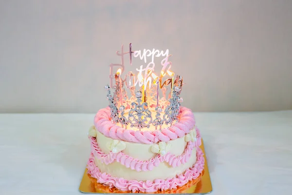 Pink and white cake with a birthday sign and a beautiful silver crown and lit candles. Select focus