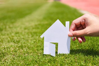 Yeşil çimen arka planındaki beyaz kağıttan elde tutulan ev modeli. Başarı rüya yaşam konsepti.