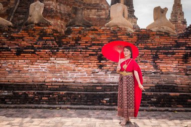 Geleneksel kırmızı Tayland elbisesi ve altın aksesuarları giyen genç kadın, tarihi Wat Chaiwatthanaram Ayutthaya sitesinde geleneksel bir şemsiye tutuyor. Tayland ulusal kostümü