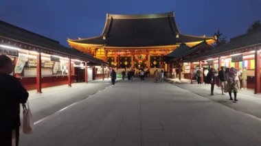 Tokyo, Japonya - 9 Nisan 2024: Sensoji Tapınağı önünde turistler ve hacılar kırmızı fenerler, ışıklar ve gece vakti kiraz çiçekleri açarken hediyelik eşya dükkanları.