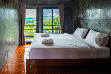 Beyaz şilteli ve yastıklı ahşap yatak odası. Dağlara ve ağaçlara bakan bir penceresi var. Doi Mae Salong 'daki yeşil çay çiftliği, Chiang Rai, Tayland.