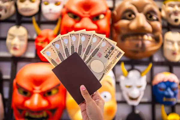 stock image Japanese 10,000 yen banknote in hand and a tourist passport are used to buy and sell goods with demon mask background of a store. Select focus