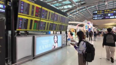 BANGKOK, THAILAND - 6 Nisan 2024: Kadın ya da kadın turist ayakta duruyor ve kalkış çizelgesine bakıyor modern dijital izleme ve Suvarnabhumi Havalimanı 'nda uçuş kartı oluşturuyorlar.