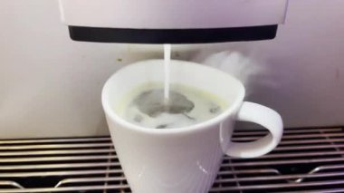 Modern bir otomatik kahve makinesi sıcak espresso yumrukluyor. Köpük ve buhar çıkıyor..