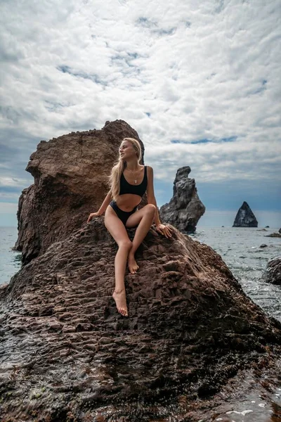 水着の海を泳ぐ女性 黒い水着の魅力的なブロンドの女性は 岩の周りの海岸の空気を楽しんでいます 旅行と休暇のコンセプト — ストック写真