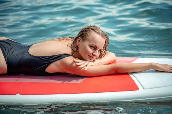 ウーマンソウの海 晴れた夏の日に海のサーフボードでスポーツガール 黒い入浴スーツで 彼は海の樹液の上に横たわっている 海に残る — ストック写真