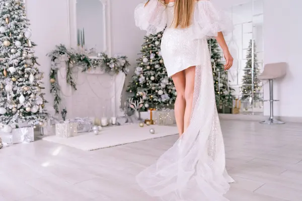 クリスマスルームのブロンド 光沢のある明るい短いドレスの美しいブロンドの女性は クリスマスツリーでお祝いのインテリアで装飾された美しい明るい部屋に立っています — ストック写真