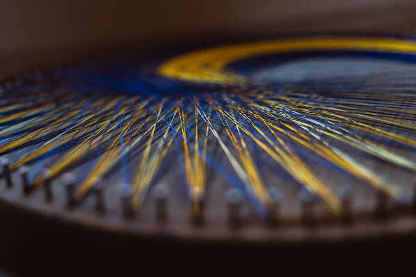 Colored thread mandala on a wooden board with nails. Mandala Moon Harmony Sun esotericism and psychology pictures from yellow and blue silk threads