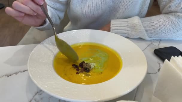 用微绿色装饰的奶油南瓜汤 一个女人在咖啡店里吃白盘里的汤 在餐馆吃午饭 在咖啡馆吃晚餐 — 图库视频影像