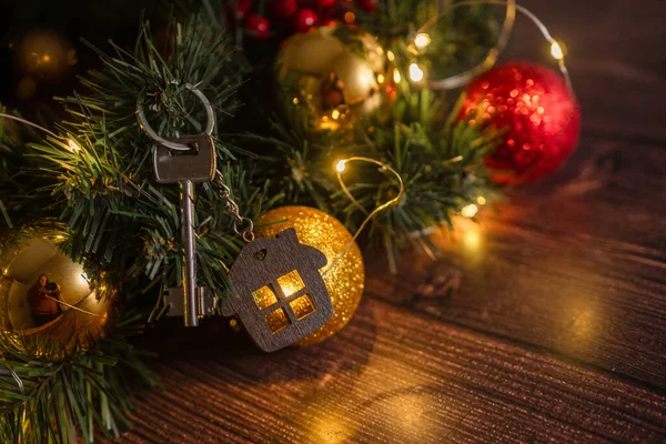 Gift key house with a keychain backdrop of Christmas tree. Building, design, project, moving to new house, mortgage, rent and purchase real estate. A gift for New Year, Christmas.