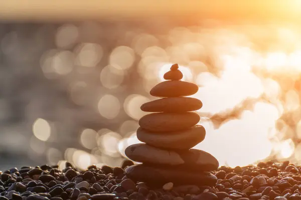Balanced rock pyramid on pebbles beach. Golden sea bokeh on background. Selective focus, zen stones on sea beach, meditation, spa, harmony, calm, balance concept