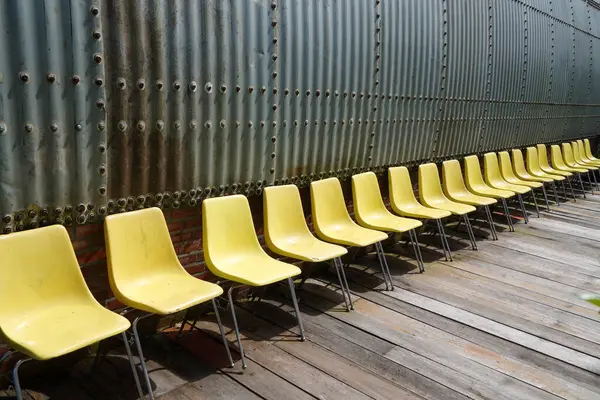 Eski sarı sandalyeler alüminyum bir çerçevenin önünde dizilmiş..