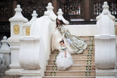 Kaliteli kıyafetler giyen iki kız kardeş büyük bir bahçe evinde mutlu mesut eğleniyorlar..