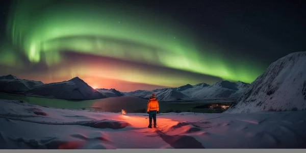 Person standing in a snowy landscape with the northern lights in the sky and a lake in front of him