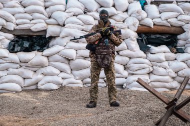 Askeri üniformalı asker, kum torbaları ve anti-tank kirpi bariyerlerinden yapılmış barikatların yanında duruyor. Barikatta bir asker var. Tam teçhizatlı bir savaşçı. Savaş kavramı