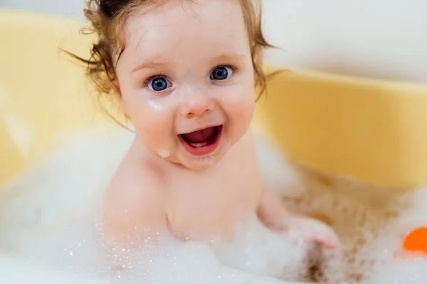 泡とシャボン玉付きのお風呂で赤ちゃんの女の子 おもちゃで遊んでいる赤ちゃんを笑って幸せ バスタブの中の小さな子供 浴室で笑顔の子供 乳児用洗浄 ストック写真
