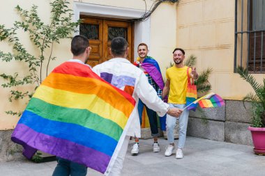 Neşeli bir grup eşcinsel arkadaş, bayraklar, çantalar ve gömlekler gibi bir dizi LGBT eşyasıyla süslenmiş başka bir çifti kapısının önünde sevinçle karşılıyor..