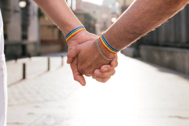 Güneşin öptüğü bir şehirde, tanınmayan iki adam el ele yürür, siluetleri titrek akşam ışığına karşı.