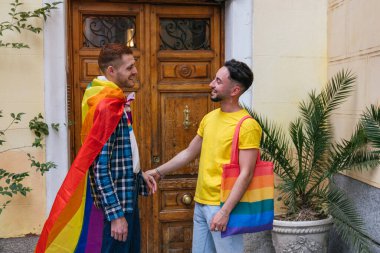 Canlı bir enstantane, el ele tutuşurken mutluluk saçan iki gay arkadaşını yakalar, evleri renkli LGBT sembolleriyle süslenir..