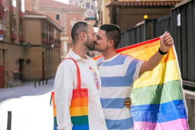 Güneşli bir şehirde, renkli LGBT aksesuarlarıyla süslenmiş romantik bir günbatımı öpücüğünü paylaşan iki eşcinsel arkadaş..