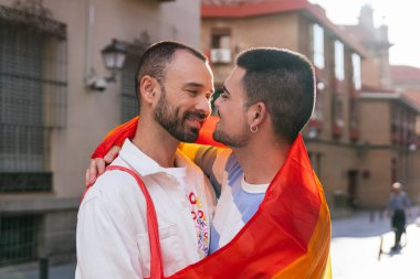 Güneşten sırılsıklam olmuş bir şehirde, iki eşcinsel arkadaş birbirine sarılıyor, birbirlerine nazik bakışlar atıyorlar, canlı LGBT sembolleriyle süsleniyorlar..